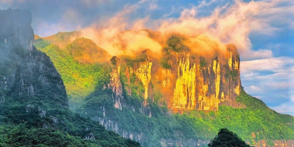 The sheer cliffs of Jinfo Mountain lit gold at sunset, with cloud over the top
